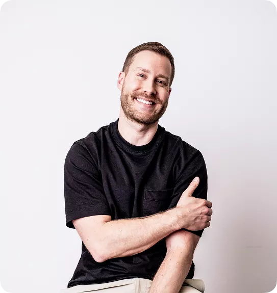 Smiling man with short hair and beard in a black t-shirt, arms crossed, testimonial photo on a light background.